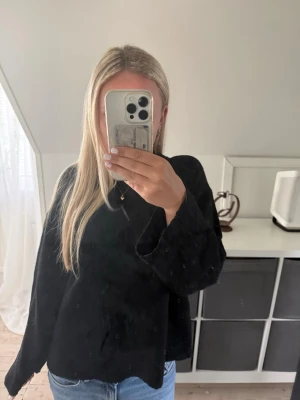 Svart oversized stickad tröja - En svart, oversized stickad tröja med rund hals och långa ärmar. Tröjan har en avslappnad passform och är perfekt att bära till jeans eller kjol. Materialet ser mjukt och bekvämt ut, vilket gör den enkel att styla till olika looks.