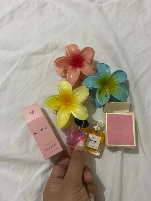 Färgglada blomformade hårklämmor plus 2st mini parfymer - Tre stora hårklämmor i form av blommor i färgerna gul, blå och rosa. Klämmorna har en glansig finish och är tillverkade i plast. Perfekta för att skapa en färgglad och lekfull look i håret.