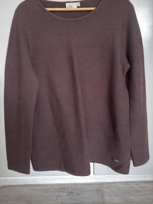 Brun stickad tröja från Isolde - Mysig brun stickad tröja från Isolde med rund halsringning och diskret ribbad struktur. Tröjan har långa ärmar och en enkel, stilren design som passar perfekt till jeans eller kjol. Ytludd finns vid armhålorna.