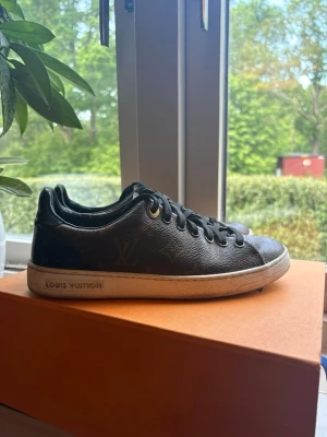 Louis Vuitton svarta låga sneakers - Snygga svarta sneakers från Louis Vuitton med klassiskt monogrammönster i brunt och guld. Skorna har svarta skosnören, vita sulor och guldfärgade detaljer vid snörningen. Tillverkade i läder med exklusiv känsla och tydlig logga på sidan av sulan. Box följer med! Storlek 35 1/5 men passar 36🩷
