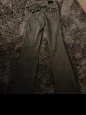 Grå bootcut jeans med fickdetaljer - Säljer ett par grå bootcut jeans med snygga fickdetaljer bak och dekorativa sömmar. Jeansen har klassisk femficksmodell och bälteshällor. Perfekta för dig som gillar en avslappnad men ändå trendig look.