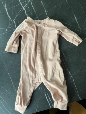 Ljusrosa pyjamas med knappar - Mysig ljusrosa pyjamas i mjukt bomullstyg med långa ärmar och ben. Helknäppt framtill med tryckknappar som går ner längs ena benet. Perfekt för sköna hemmakvällar eller som sovplagg.