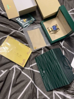 Klocka - Säljer en lyxig R klocka med blå urtavla och guldfärgade detaljer. Armbandet är i silver och guldtonat metall. Kommer med originalbox, putsduk och tillbehör. Perfekt för dig som vill ha något exklusivt på handleden.