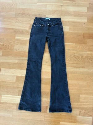 Svarta bootcut jeans med låg midja - Säljer ett par svarta bootcut jeans med låg midja och klassisk femficksdesign. Jeansen har utsvängda ben och stängs med knapp och dragkedja. Perfekta för en trendig och avslappnad stil.
