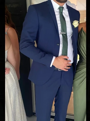 Kostym  - Snygg marinblå kostym med matchande kavaj och byxor. Kavajen har två knappar och klassisk passform. Bärs med vit skjorta och grön slips med prickigt mönster. Perfekt för dig som vill ha en stilren och modern look. Tiger of sweden, nypris 6000 säljer för 2500