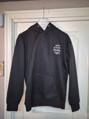 Svart hoodie Anti Social Social Club - Säljer en svart hoodie från Anti Social Social Club x PLAY med vit text och röda hjärtan på bröstet. Hoodien har huva med dragsko och en stor magficka. Perfekt för dig som gillar streetwear och vill sticka ut lite extra.