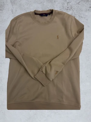 Beige sweatshirt från Polo Ralph Lauren - Snygg beige tröja från Polo Ralph Lauren med en snygg detalj på armen. Överlah en skitsnygg tröja som passar till alla slags tillfällen. Bara att skriva ifall det finns några funderingar, och som sagt priset går alltid att diskutera!