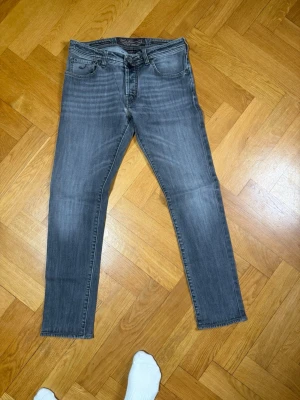 Grå slim fit jeans Jacob Cohen 622 - Snygga grå slim fit jeans från Jacob Cohen 622  med klassisk femficksmodell och subtila slitningar. Jeansen har en diskret logga på myntfickan och är tillverkade i mjuk denim med stretch för extra komfort.
