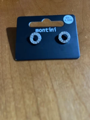 Silverfärgade cirkelörhängen Montini - Snygga örhängen från Montini i silverfärg med cirkelformad design. Örhängena är dekorerade med små gnistrande stenar som ger en elegant touch. Perfekta för att lyfta din stil med lite extra bling.