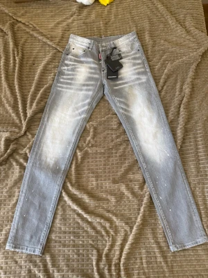 Ljusgrå skinny jeans Dsquared2 - Säljer ett par ljusgrå skinny jeans från Dsquared2 med coolt blekta partier och vita färgstänk. Jeansen har klassisk femficksmodell, låg midja och smal passform. Materialet är stretchigt denim för extra komfort. Perfekta för dig som vill sticka ut med din stil.