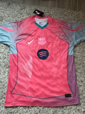 Barça rosa matchtröja Nike - Snygg rosa och ljusblå FC Barcelona matchtröja från Nike med klubbmärke och Spotify-logga på bröstet. Tröjan har korta ärmar, rund hals och är tillverkad i ett lätt, ventilerande material perfekt för träning eller match. Storlek XL men passar M också