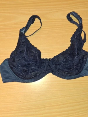 Mörkblå spets-bh med bygel - Snygg mörkblå bh med bygel och spetsdetaljer. Bh:n har justerbara axelband och hakknäppning bak. Kuporna är dekorerade med blommig spets och ger ett elegant intryck. Perfekt för dig som gillar en klassisk och stilren look.