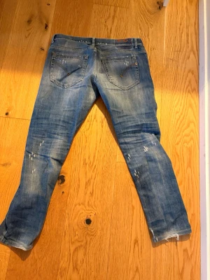 Blå slim jeans från dondup - Säljer ett par blå slim fit jeans från Dondup med slitningar och färgstänk för en cool, avslappnad look. Jeansen har klassiska bakfickor med dekorativa sömmar och en ljus tvätt. Perfekta för dig som gillar streetstyle.