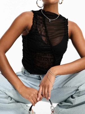Svart mesh och spets topp från ASOS - Säljer en svart ärmlös topp från ASOS DESIGN i mesh och spets. Toppen har asymmetrisk design med transparenta partier och snygga rynkade detaljer. Perfekt för dig som vill ha en edgy och trendig look.