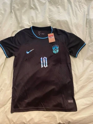 Svart Brasilien Neymar Jr Nike tröja - Endast en intressekoll! Snygg svart Brasilien fotbollströja från Nike med Neymar Jr och nummer 10 i blått och vitt på ryggen. Tröjan har blå detaljer vid krage och ärmslut samt Brasilien-emblem på bröstet. Perfekt för fotbollsfans som vill sticka ut.