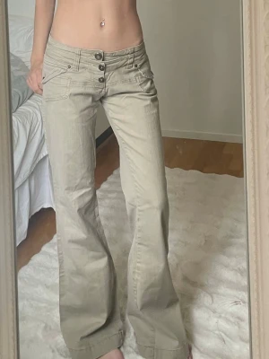 Beiga vida jeans med knappar - Snygga beiga byxor med låg midja och vida ben. Byxorna har flera dekorativa knappar framtill och fickor både fram och bak. Perfekta för en avslappnad och trendig look. Storlek XS, jag är 166 cm