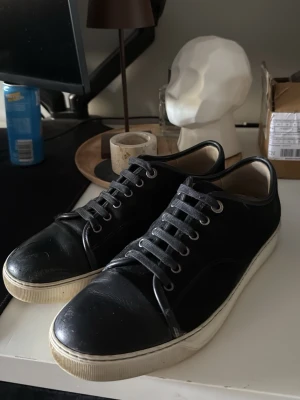 Svarta sneakers med vit sula, Lanvin  - Snygga svarta sneakers med lågt skaft och vit sula. Ovandelen är i en mix av mocka och slätt läder, med svarta skosnören och metallfärgade öljetter. Klassisk och stilren design som passar till det mesta. Det är ett litet slitage på högra skon men inget större. Annars väldigt fräscha och rena. Man får med box osv som man kan se på bilderna! Pris kan diskuteras 