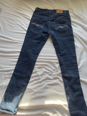 Mörkblå jeans från Nudie Jeans - Säljer ett par mörkblå jeans från Nudie Jeans med klassisk femficksdesign och kontrastsömmar. Jeansen har raka ben och detaljerade bakfickor med Nudie Jeans signaturbrodyr. Materialet är mjukt denim i bomull. Pris kan diskuteras vid snabb affär, Storlek W29 L34, för mer frågor är det bara att höra av sig mvh Hjalle!☀️