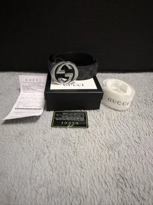 Svart Gucci skärp med GG-spänne - Snyggt svart skärp från Gucci med klassiskt GG-mönster och stort, silverfärgat GG-spänne. Skärpet är gjort i skinn och har en exklusiv känsla som lyfter vilken outfit som helst. Perfekt accessoar för dig som gillar lyxiga detaljer.