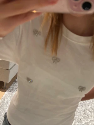 Vit t-shirt med strassrosetter - Supersöt vit t- shirt med diamant rosetter! Superfin och aldrig använd🩷fråga gärna om fler bilder och pris kan diskuteras🫰🏻passar mig som brukar ha xs/xxs!