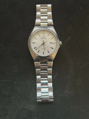 Silverfärgad klocka från Festina - Stilren klocka från Festina med silverfärgat armband i metall och vit urtavla. Klockan har datumvisning och klassisk design med länkarmband och tydliga markeringar. Perfekt accessoar för dig som gillar en clean look.