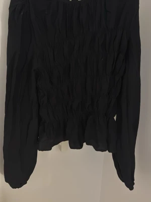 Svart långärmad blus från Nelly💗 - Trendig svart smockad blus från Nelly med långärmad design och smockad front. Tillverkad i ett lätt och luftigt tyg som ger en snygg struktur. Perfekt att matcha med både jeans och kjol för en stilren look. Använd 1 gång så är som ny i skicket!💕💕hör gärna av er vid intresse eller om ni har några frågor!💕