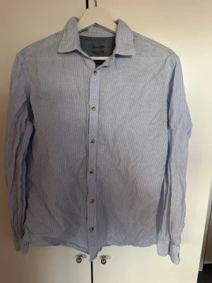 Blårandig skjorta från Essentails - Klassisk blårandig skjorta från Essentials med krage och långa ärmar. Skjortan har knappar framtill och är tillverkad i bomull för en skön och luftig känsla. Perfekt till jeans eller chinos för en clean look. Storlek M