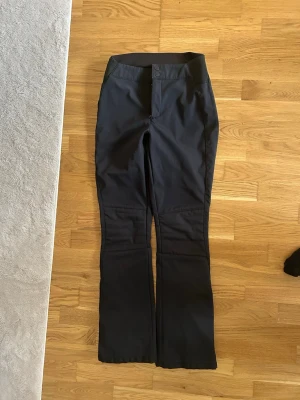  EVEREST Softshell skidbyxor dam strl 36 - Säljer ett par svarta täckbyxor med bootcut-modell och hög midja. Byxorna har dubbla knappar i midjan och är tillverkade i ett slitstarkt, vattenavvisande material. Perfekta för kalla dagar och outdoor-aktiviteter.
