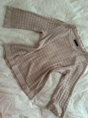 Rosa rutmönstrad tröja  - Snygg beige tröja  med rutigt mönster och breda ribbade kanter vid ärmslut och nederkant. Tröjan har rund halsringning och är tillverkad i ett mjukt, stickat material. Perfekt för en chill och stilren look.