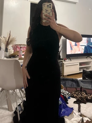 Svart långklänning med slits - Snygg svart långklänning med hög halsringning och ärmlös design. Klänningen har en figurnära passform och en slits på sidan som ger en extra touch. Perfekt för dig som vill ha en stilren och elegant look. Storlek S