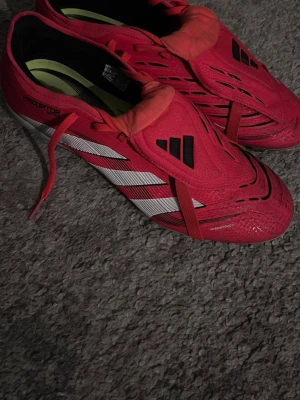 Adidas Predator röda fotbollsskor - Använda 3 gånger, köpta för 2000 Säljer ett par röda Adidas Predator fotbollsskor med vita och svarta detaljer. Skorna har klassisk snörning, täckt plös och ikoniska tre ränder på sidan. Tillverkade i syntetmaterial för bra grepp och kontroll på planen. Perfekta för dig som vill sticka ut på matchen.