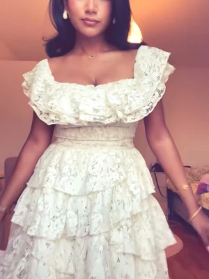 Vit spetsklänning med volanger Studenten - Studentklänning med flera lager volanger och breda axelband. Klänningen har spetsdetaljer och en omlottliknande överdel. Bara använd en gång och blev inte champangead så den är inte äcklig på nått sätt!