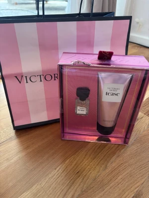 Victoria's Secret Tease presentset - Snyggt presentset från Victoria's Secret med doften Tease. Setet innehåller en parfymflaska och en matchande bodylotion, båda i rosa och svart design. Kommer i en lyxig rosa presentförpackning med glansiga detaljer och en söt rosett på toppen.