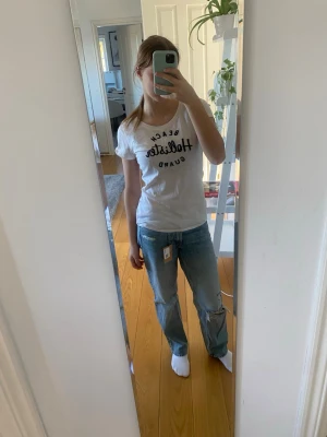 Blå low waist baggy jeans med slitningar - Säljer ett par ljusblå baggy jeans med slitningar på knäna och lös passform. Jeansen har klassisk femficksdesign och raka ben. Perfekta för en avslappnad och trendig look.