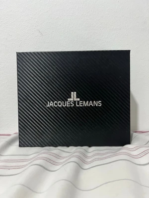 Jacques Lemans silverfärgad klocka - Snygg klocka från Jacques Lemans i silverfärgat stål med svart urtavla och kronograf. Kommer i originalbox med extra svart läderarmband. Köpt för 1700kr går nu för 1200 pris kan diskuteras. Den är aldrig använd