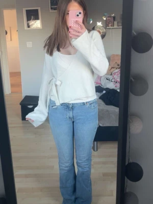 Vit omlottkofta med knytband - Snygg vit omlottkofta med knytband i sidan och långa ärmar. Koftan har en avslappnad passform och är gjord i ett mjukt, stickat material. Perfekt att styla över ett linne eller t-shirt för en trendig lager-på-lager-look.