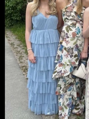 Ljusblå balklänning - Säljer en lång, ljusblå balklänning med flera lager volanger och smala axelband. Klänningen har v-ringad urringning och är tillverkad i ett lätt, luftigt material. Perfekt för skolbal eller bröllop. Jag på bilderna är ca 155-157cm. Och passar någon runt den längden. Den har justerbara band och en dragkedja ända ner till svanken. Superfin och skön!💙