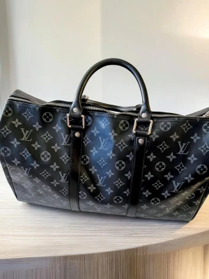 Iouis Vuitton resväska  - Säljer en ikonisk reseväska i en elegant mörkgrå och svart färgkombination med det karaktäristiska mönstret. Detta är den perfekta följeslagaren för både weekendresor och som lyxigt handbagage på flyget.