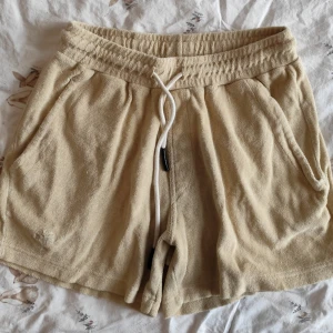 OAS Terry shorts - Mysiga beige shorts i frotté med elastisk midja och vit snörning framtill. Två sidofickor och en bakficka ger en avslappnad look. Perfekta för varma dagar eller chill hemma.