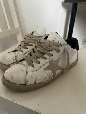 Golden goose skor - Golden Goose sneakers i vitt läder med beige mockadetaljer och en ikonisk grå stjärna på sidan. Skorna har beige snören, svart hälparti och en vintage-inspirerad look. Perfekta för dig som gillar streetstyle och unika detaljer.