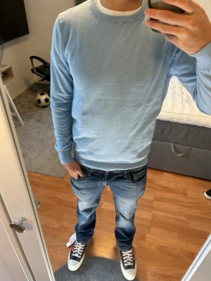 Ljusblå stickad tröja Brothers - Snygg ljusblå stickad tröja från Brothers med rund halsringning och ribbade muddar vid ärmslut och nederkant. Perfekt för lager-på-lager och enkel att matcha med jeans eller chinos. Mjuk och tunn kvalitet som känns skön mot huden.