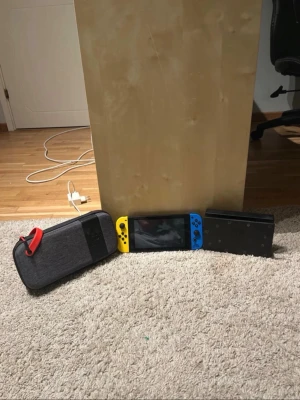 Nintendo Switch konsol med tillbehör - Nintendo Switch konsol med neonblå och neon-gul Joy-Con, svart dockningsstation och en grå bärväska med röd dragkedja. Perfekt för gaming hemma eller på språng, stilren design och smidigt format.