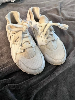 Nike huarache - Säljer ett par vita Nike Air Huarache sneakers med klassisk chunky sula och meshdetaljer. Skorna har låga skaft, breda snören och en mix av syntet och textilmaterial. Perfekta för dig som gillar sportig och clean stil.