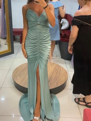 Mintgrön lång klänning Sibel Aydin - Helt ny med prislapp. Elegant mintgrön lång klänning från Sibel Aydin med smala axelband, draperad framsida och hög slits. Klänningen har figurnära passform och är tillverkad i ett glansigt, satinliknande material som ger en lyxig känsla. Kedja som är avtagbar 