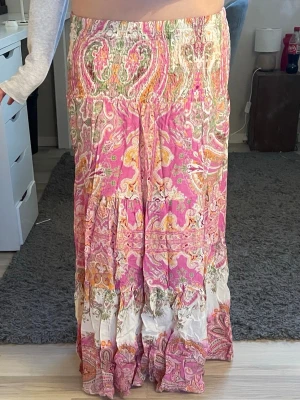 Färgglad långkjol med paisleymönster - Säljer en bohemisk långkjol i rosa, orange, grön och vit med paisleyinspirerat mönster. Kjolen har resår i midjan och är tillverkad i ett lätt, skönt material som passar perfekt till varmare dagar. Flödande och luftig passform.