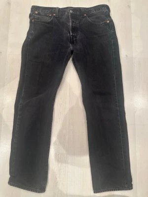 Svarta Levi's 501 jeans straight fit W30 L30 - Klassiska svarta Levi's 501 jeans med rak passform och femficksdesign. Jeansen har knappgylf och är tillverkade i robust denim. Perfekta för en stilren och tidlös look.