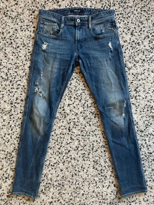 Replay Anbass - Säljer ett par blå jeans från Replay, modell Anbass. De har snugg tvätt och slitningar för en trendig look. Klassisk femficksmodell med dragkedja och knapp. Width: 29 Length 32