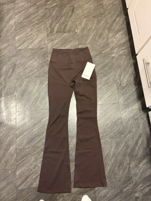 Bruna flared leggings från Lululemon - Supersnygga bruna leggings från Lululemon med hög midja och utsvängda ben. Tillverkade i ett mjukt och stretchigt material som sitter skönt på kroppen. Perfekta för dig som gillar en trendig och bekväm look.