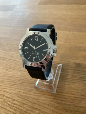Vintage Les Parfums 40mm Unisex - Säljer ett ovanligt 40mm armbandsur från franska Les Parfums. Klockan har ett svart läderarmband och en silverfärgad boett med svart urtavla. Urtavlan har romerska siffror vid klockan 12 och 6. Klockan drivs av ett kvartsurverk. Fint skick enligt bilder. Behöver nytt batteri.  Mitt pris: 289 SEK  Skickas alltid snabbt och spårbart. Skriv vid frågor och se gärna mina andra annonser!   GRATIS: För återkommande kunder erbjuder jag personlig experthjälp för dig att göra nya fynd (nytt & begagnat). F