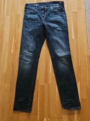 G-Star Holmer - Snygga mörkblå slim fit jeans med slitningar och knäppning fram med fyra synliga knappar. Jeansen har klassiska fem fickor och kontrastsömmar. Materialet är denim i bomull. Perfekta för en trendig och avslappnad stil.
